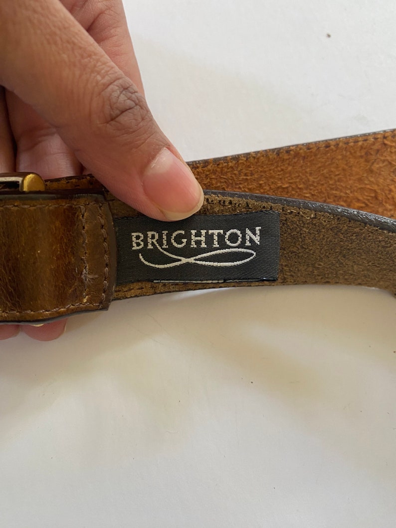 May include: A brown leather belt with a gold buckle and a black label that reads "BRIGHTON".