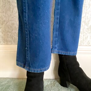 May include: A pair of blue denim jeans with a slight flare at the bottom. The jeans are worn with black ankle boots.