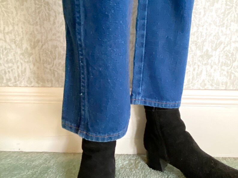May include: A pair of blue denim jeans with a slight flare at the bottom. The jeans are worn with black ankle boots.