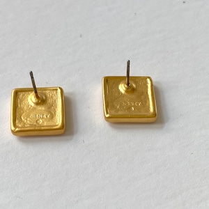 May include: A pair of gold-tone square-shaped earrings with a post back. The back of the earrings are stamped with the word "DISNEY".