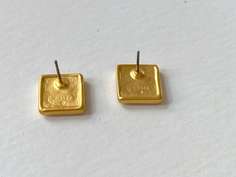 May include: A pair of gold-tone square-shaped earrings with a post back. The back of the earrings are stamped with the word "DISNEY".