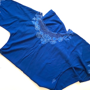 May include: A royal blue short-sleeved top with white crocheted floral embroidery around the neckline and on the sleeves.