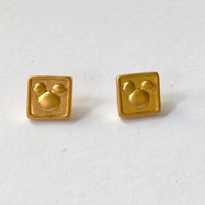 May include: A pair of gold-tone earrings with a square shape and a Mickey Mouse head design.