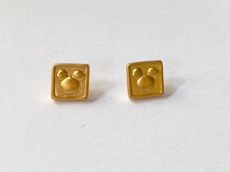 May include: A pair of gold-tone earrings with a square shape and a Mickey Mouse head design.