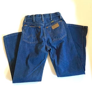 May include: A pair of blue denim jeans with a brown leather patch on the back pocket that says "Wrangler".