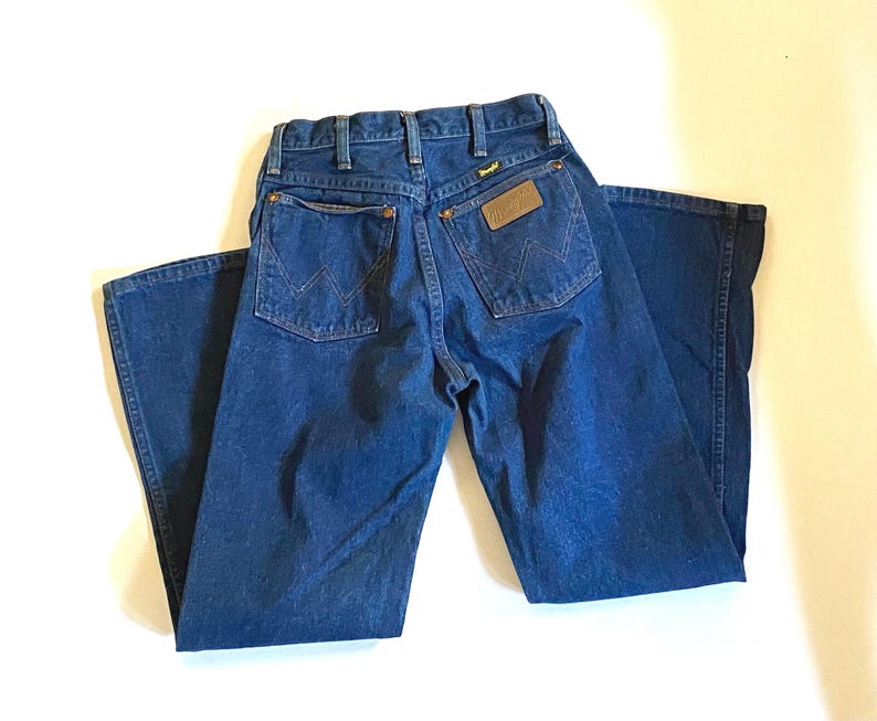 May include: A pair of blue denim jeans with a brown leather patch on the back pocket that says "Wrangler".