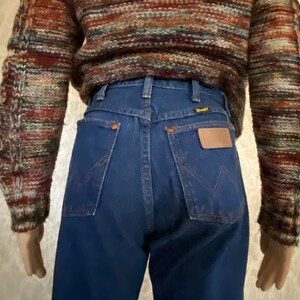 May include: A pair of dark blue denim jeans with a high waist and a back pocket with a brown leather patch that says "Wrangler".
