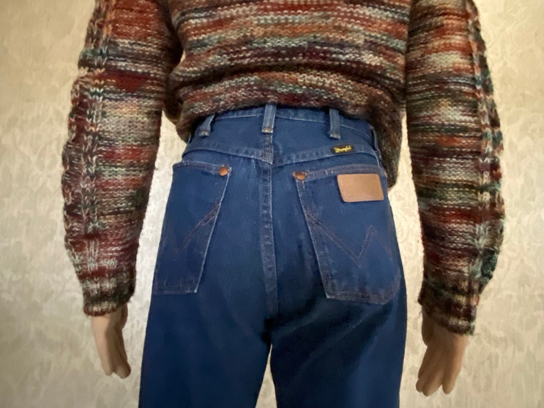 May include: A pair of dark blue denim jeans with a high waist and a back pocket with a brown leather patch that says "Wrangler".