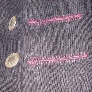 May include: Black fabric with pink stitching. The fabric has a series of decorative stitches in a zig-zag pattern.