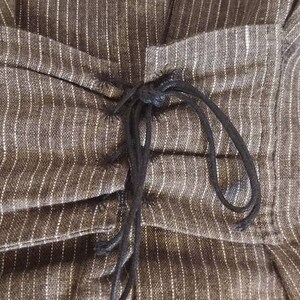 May include: A close-up of a brown and white striped fabric with a black drawstring detail. The fabric is gathered at the waist and the drawstring is tied in a knot.