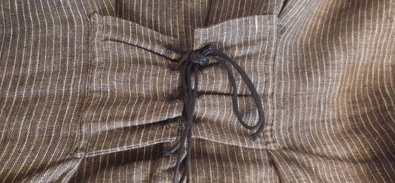 May include: A close-up of a brown and white striped fabric with a black drawstring detail. The fabric is gathered at the waist and the drawstring is tied in a knot.