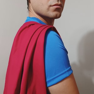 以下が含まれることがあります： 青いシャツに赤いマント。マントは鮮やかな赤色で、シャツの明るい青色と対照的です。この画像は、コスプレやテーマのあるイベントに最適な、スーパーヒーローのコスチュームを示唆しています。