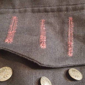 May include: A black fabric jacket with a pocket featuring three red stitched lines. The jacket has three silver buttons.