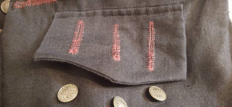 May include: A black fabric jacket with a pocket featuring three red stitched lines. The jacket has three silver buttons.