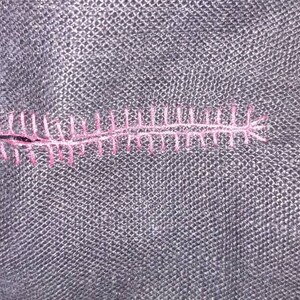 May include: Close-up of a black fabric with a pink stitched seam.
