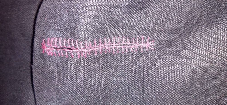 May include: Close-up of a black fabric with a pink stitched seam.