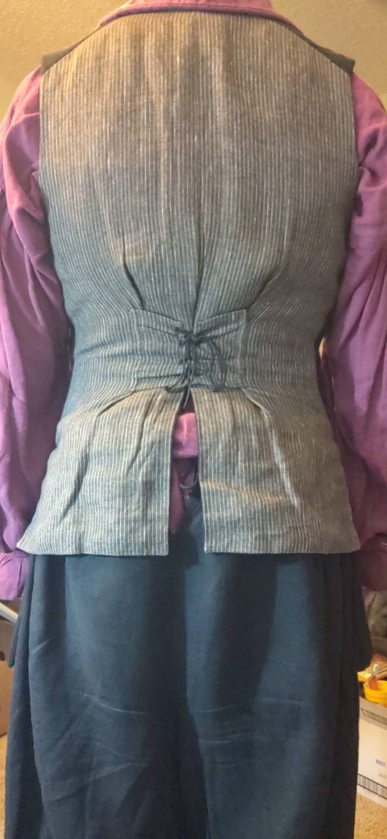 May include: A gray and white striped vest with a black lace-up back. The vest is made of a linen-like fabric and has a fitted silhouette.