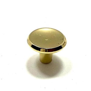 May include: A gold-colored cabinet knob with a rounded top and a cylindrical base. The knob has a shiny, reflective surface and is set against a white background. The hardware is likely for furniture.