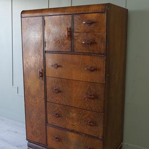 May include: A tall wooden wardrobe and chest of drawers combination piece featuring a rich brown wood grain finish. The unit includes one full-length vertical door on the left, two smaller upper drawers, and four wide lower drawers with dark handles.