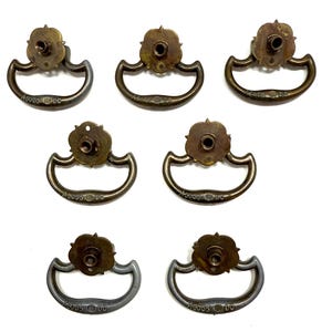 May include: Seven antique drawer pulls with a floral design and a D-shaped handle. The pulls are in various shades of brass and silver, with the text "45055 DC" visible on the handle.