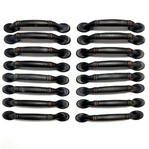 May include: A collection of 16 bronze-colored cabinet handles. Each handle has a curved design with a central, textured section and rounded ends. The handles are arranged in two columns on a white background.