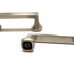 May include: Two brushed nickel cabinet pulls. Each pull has a rectangular bar with curved, square-shaped ends. The pulls are designed for easy installation and add a modern touch to cabinets or drawers. The hardware is shown against a white background.