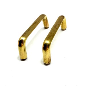 May include: Two vintage brass cabinet pulls with a curved handle design. The pulls have a golden finish and are set against a white background. Each pull measures approximately 4 inches in length.