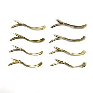 May include: Eight antique brass-colored drawer pulls with a curved, leaf-like design. Each pull features a slender, arched handle with a decorative, pointed end. The hardware is arranged on a white background.