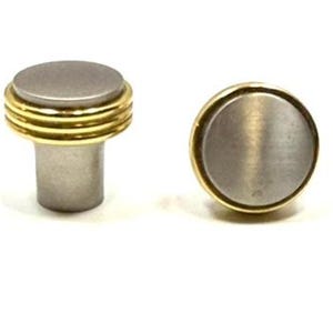 May include: Two cabinet knobs featuring a cylindrical base and a flat circular top. The hardware is constructed from a combination of brushed silver-toned metal and polished gold-toned metal, with three distinct gold rings encircling the top edge.