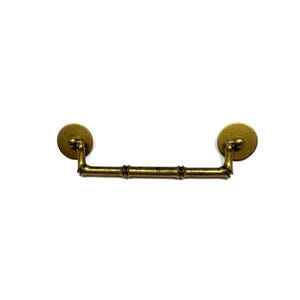 May include: Antique brass drawer pull with a bamboo-style handle. The pull has two round backplates and a curved handle with bamboo-like detailing. The hardware is a warm, aged brass color, perfect for vintage furniture restoration.