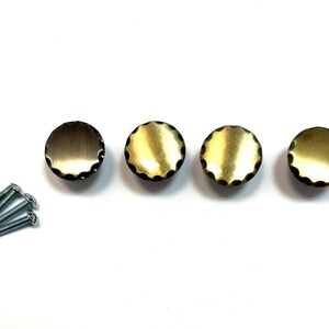 May include: Four round brass cabinet knobs with a scalloped edge and mounting screws. The knobs have a warm, golden hue and a textured surface. These decorative knobs are ideal for updating furniture.
