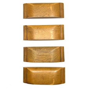 May include: Four rectangular wooden napkin rings with rounded edges are arranged vertically against a white background. The rings have a warm, light brown color and a visible wood grain texture, suggesting a natural finish.