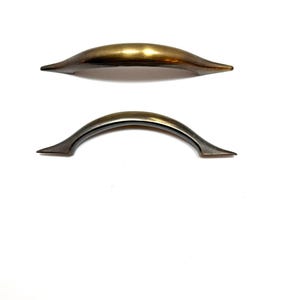 May include: Two metal cabinet pulls. The top pull is a light gold color, and the bottom pull is a darker bronze color. Both pulls have a curved design with pointed ends. The pulls are set against a white background.