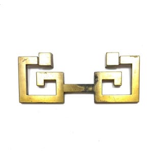 May include: A vintage brass drawer pull with a geometric design. The pull features a rectangular shape with square accents and a connecting bar. The brass has a warm, aged patina, suggesting its vintage origin.