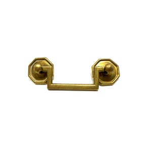 May include: A vintage-style brass drawer pull with an octagonal backplate and a rectangular handle. The hardware has a warm, golden hue and is designed for furniture restoration or decorative purposes.