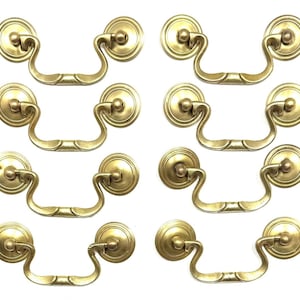 May include: Eight antique brass drawer pulls. Each pull features a circular backplate and a curved handle. The brass hardware is a warm gold color, perfect for adding a vintage touch to furniture. The pulls are shown against a white background.