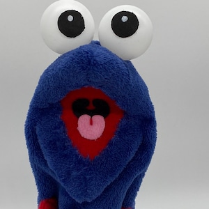 May include: A whimsical, plush creature with large white eyes and black pupils. The creature has a blue, textured body with a red mouth and a pink tongue. The overall design is playful and cartoonish.