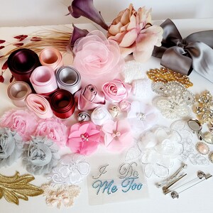 May include: Assortment of craft supplies for wedding decorations, including pink, white, and gray fabric flowers, lace, ribbon, and embellishments. The text "I Do Me Too" is visible on a clear sticker.