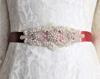 May include: A white lace dress with a red satin sash and a pearl and rhinestone embellished belt.