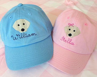 May include: Two personalized baseball caps with embroidered yellow labrador retriever images. The blue cap says "William" and the pink cap says "Stella".