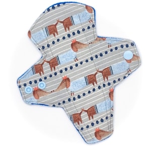 May include: A gray and blue reusable cloth menstrual pad with a pattern of dachshunds wearing blue shirts and crowns. The pad has blue snaps on the sides.
