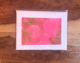 Op de afbeelding: Een roze en gouden abstracte kunstprint op een witte kaart. De print heeft een marmereffect met swirls van roze en gouden verf.