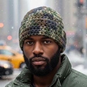 May include: A person wearing a green puffer jacket and a camouflage knit beanie in a snowy urban setting. The jacket has a button and zip closure. The beanie features shades of green, brown, and blue.