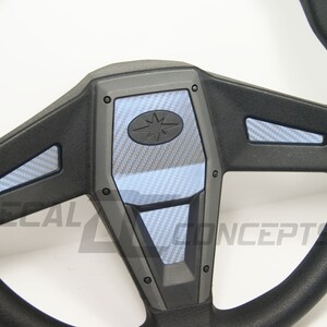 May include: A black steering wheel with a carbon fiber pattern on the spokes and center. The center piece has a star logo.