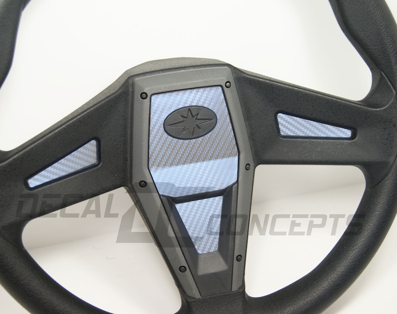 May include: A black steering wheel with a carbon fiber pattern on the spokes and center. The center piece has a star logo.