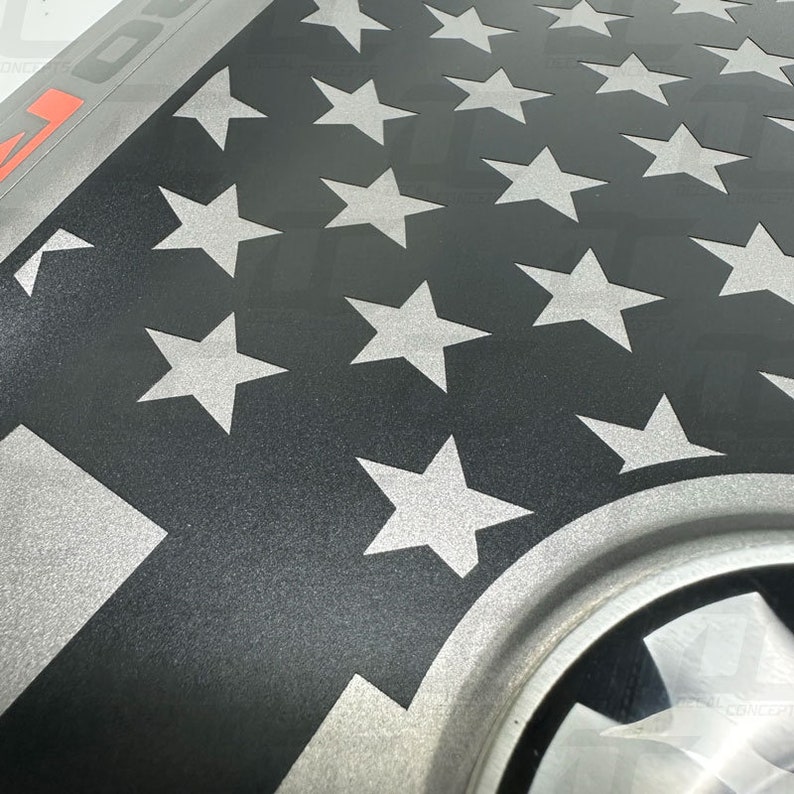 May include: A black and silver American flag decal with a white stripe and a silver star pattern. The decal is designed to be applied to a vehicle.