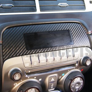 以下が含まれることがあります： カーボンファイバーのトリムが付いた車のダッシュボード。ダッシュボードには、ラジオ、CD、電話機能のボタンが付いたセンターコンソールがあります。トリムは黒とグレーの織り模様です。ダッシュボードには、通気孔とコントロールノブもあります。