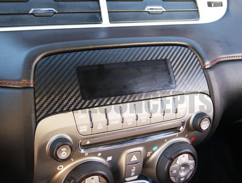 以下が含まれることがあります： カーボンファイバーのトリムが付いた車のダッシュボード。ダッシュボードには、ラジオ、CD、電話機能のボタンが付いたセンターコンソールがあります。トリムは黒とグレーの織り模様です。ダッシュボードには、通気孔とコントロールノブもあります。