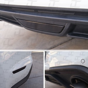 Könnte beinhalten: Ein weißes Auto mit schwarzem Zierleisten um den hinteren Stoßfänger. Der Stoßfänger hat einen schwarzen Reflektor auf der linken Seite und einen schwarzen Diffusor auf der rechten Seite.