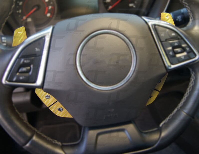May include: A black leather steering wheel with yellow carbon fiber accents. The steering wheel has buttons on the left side and a plus and minus button on the right side.